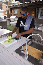 Man preparing food outdoors with a grill and sink in the background