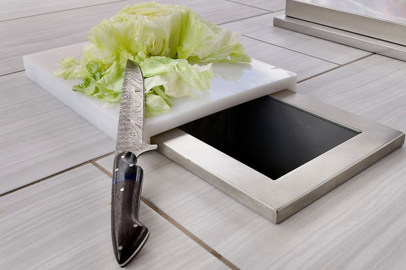 Knife on a cutting board with lettuce, next to a small stove on a wooden surface