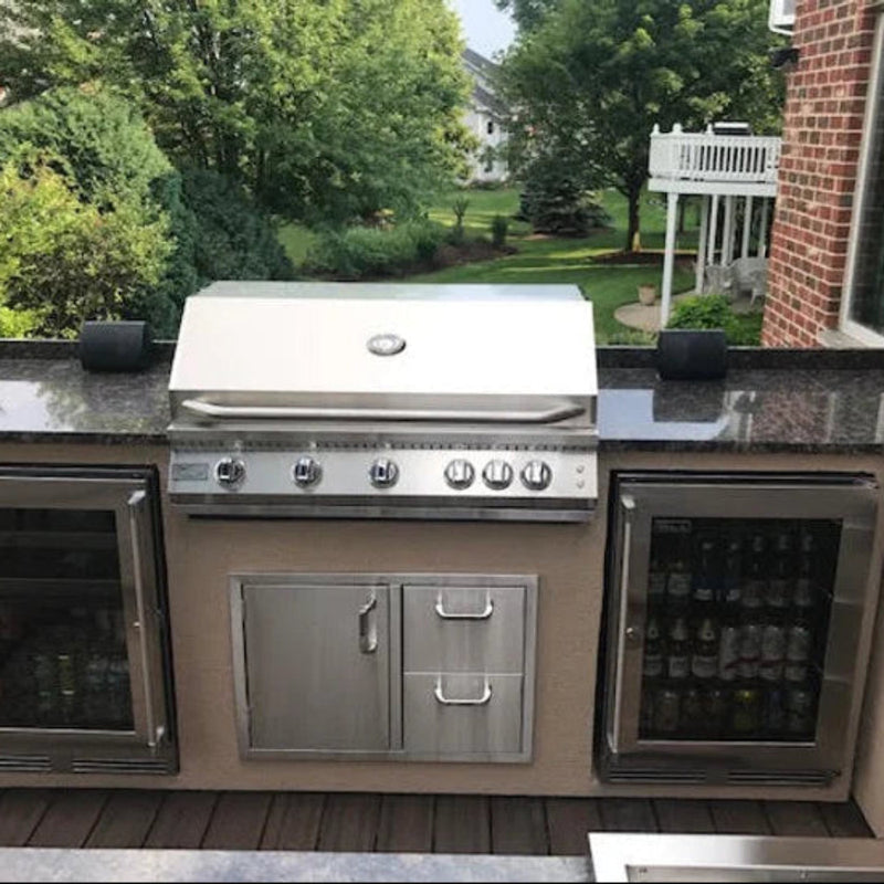 Outdoor kitchen with stainless steel grill and beverage cooler on a patio