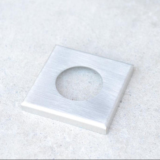 Metallic square with circular hole on a textured white surface