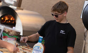 Person preparing food outdoors with a pizza oven in the background